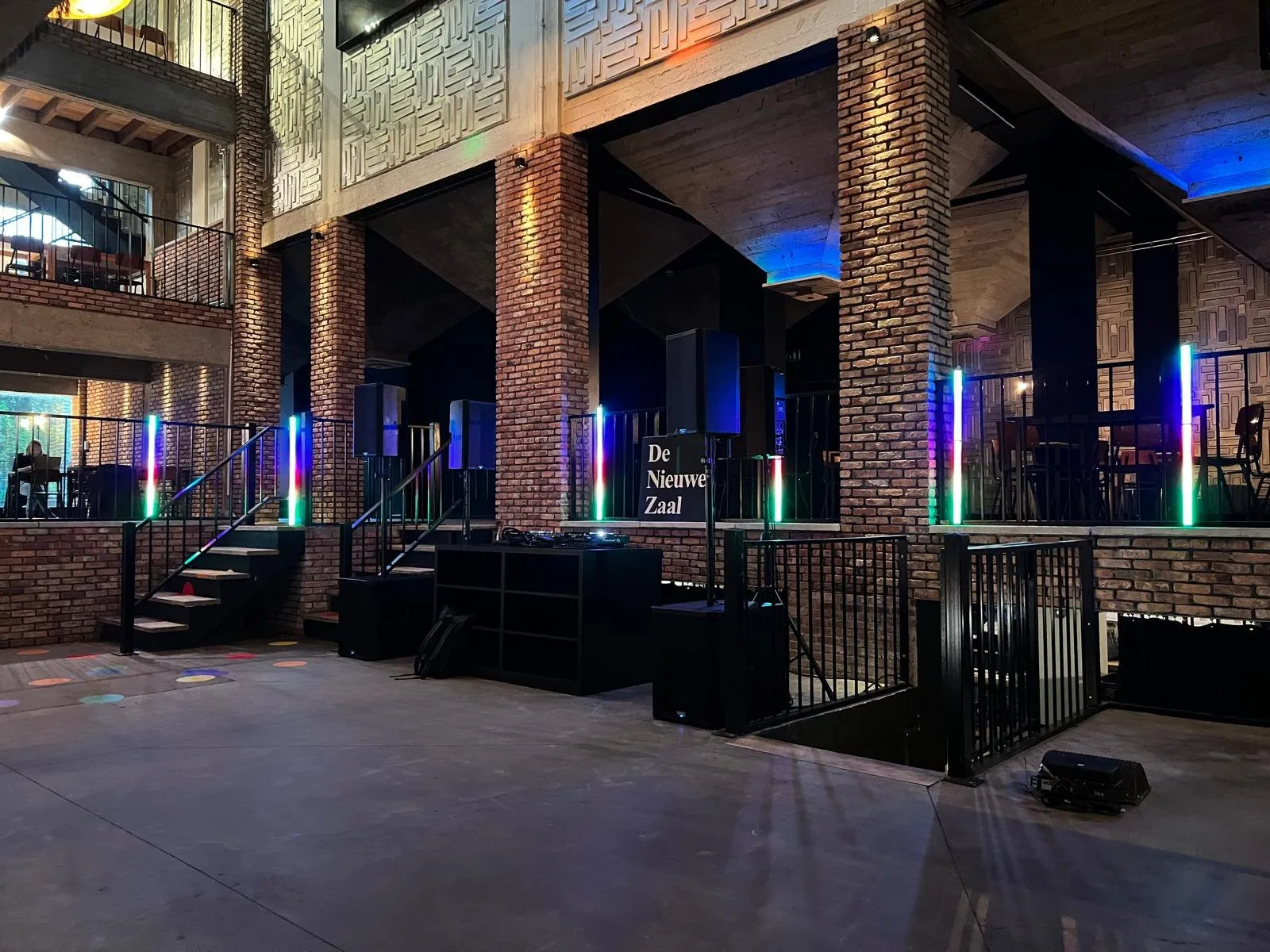 Industriële zaal met bakstenen pilaren en een DJ-booth op een verhoog