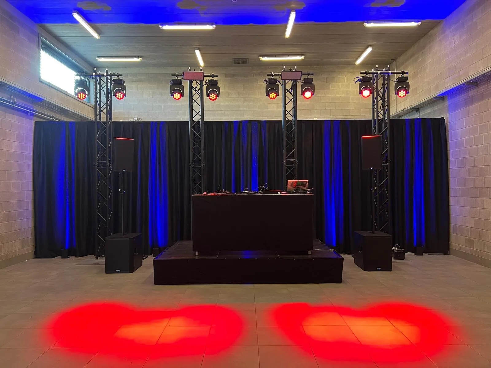 DJ-podium met truss, blauwe gordijnen en rode spots
