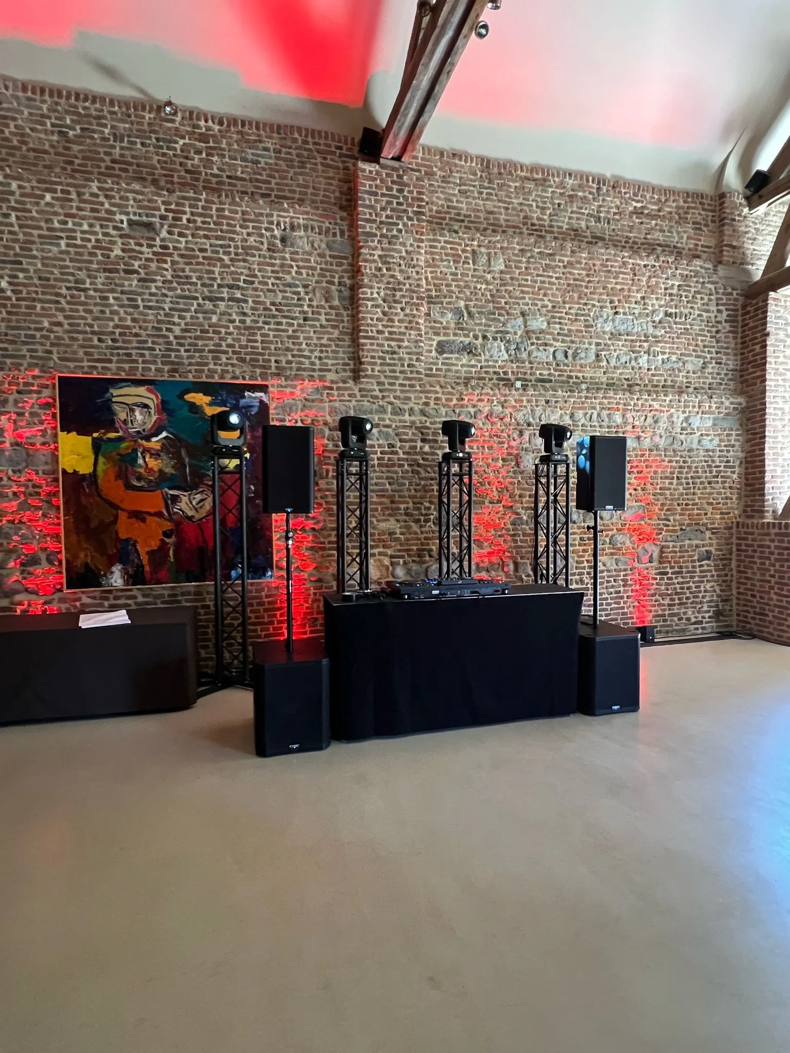 DJ-booth met rode uplights in een zaal met bakstenen muren