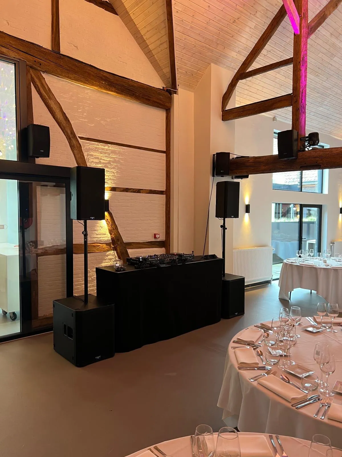 DJ-opstelling in een schuur met houten balken, naast de gedekte tafels