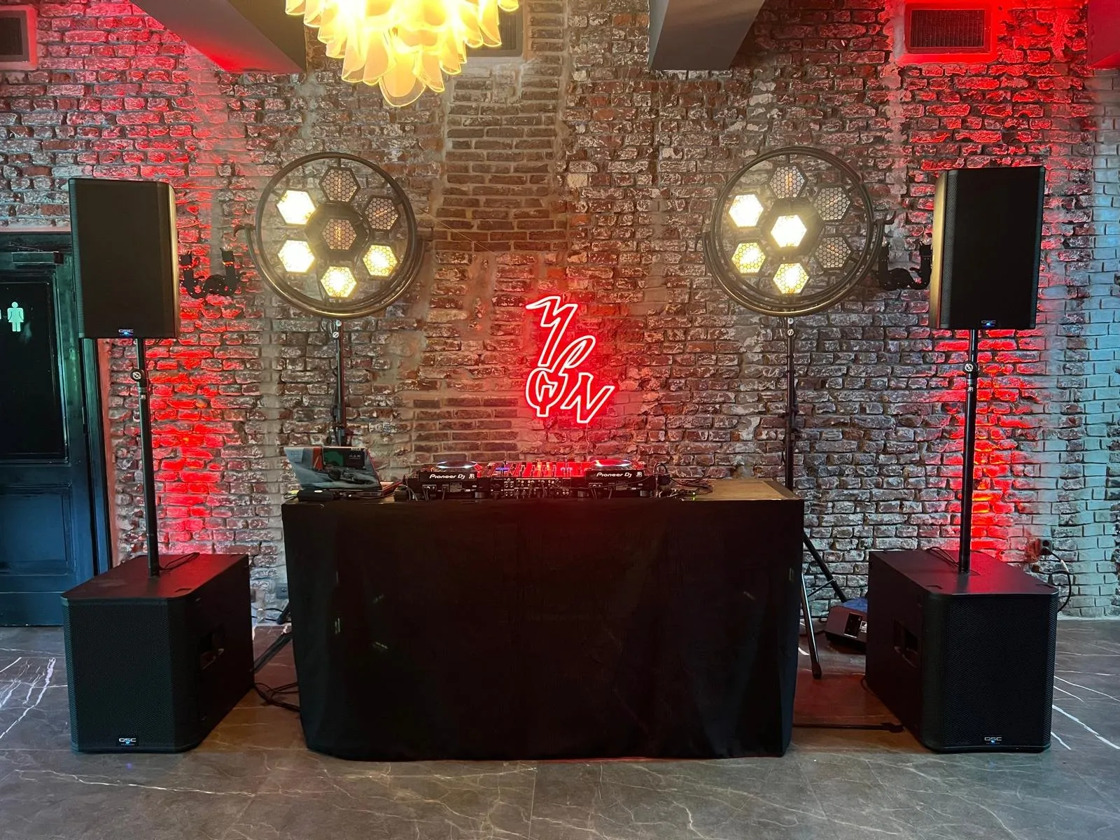 DJ-booth met neonlicht en rode uplights tegen een bakstenen muur